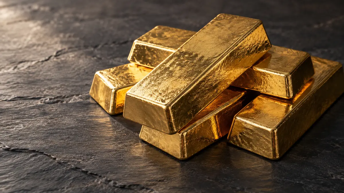Several unmarked gold bars on a dark slate surface with soft natural side lighting